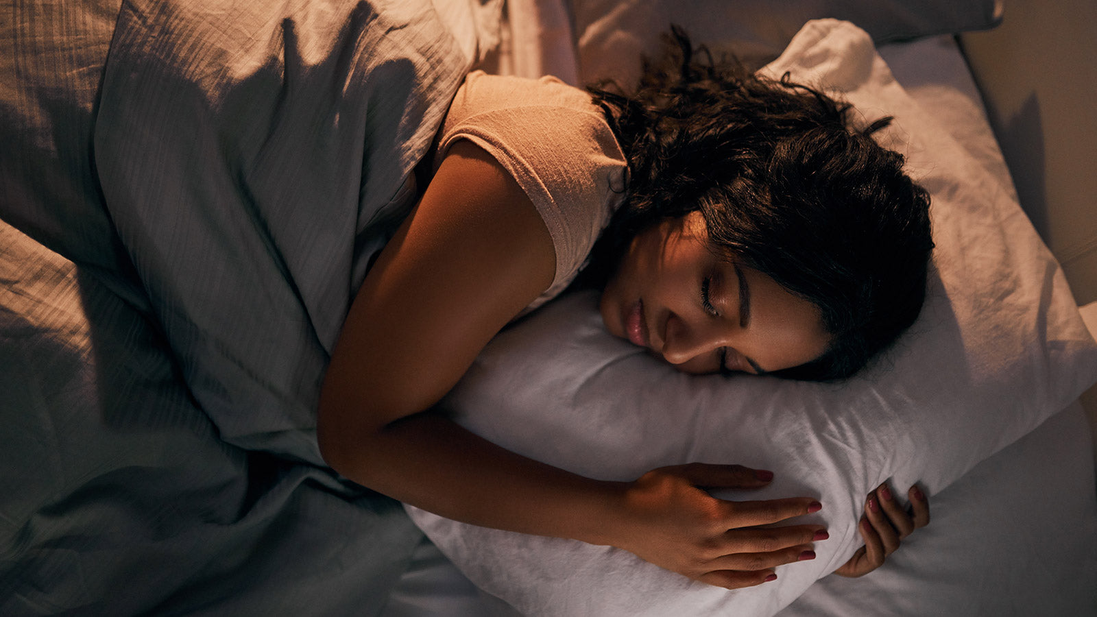 Women sleeping peacefully while wrapped in blankets and hugging her pillow