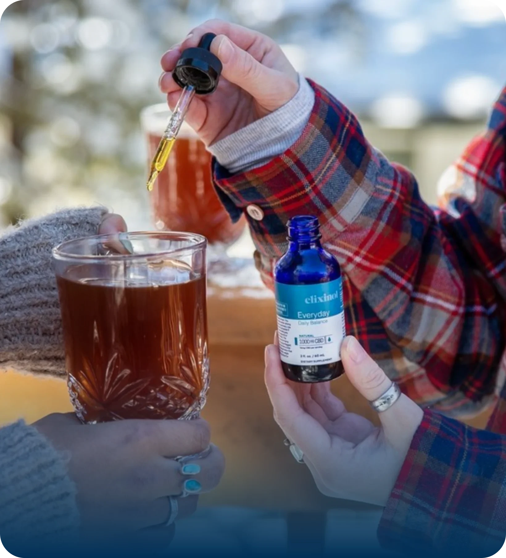 A hand holding a tincture pipette and adding drops to a cup of tea