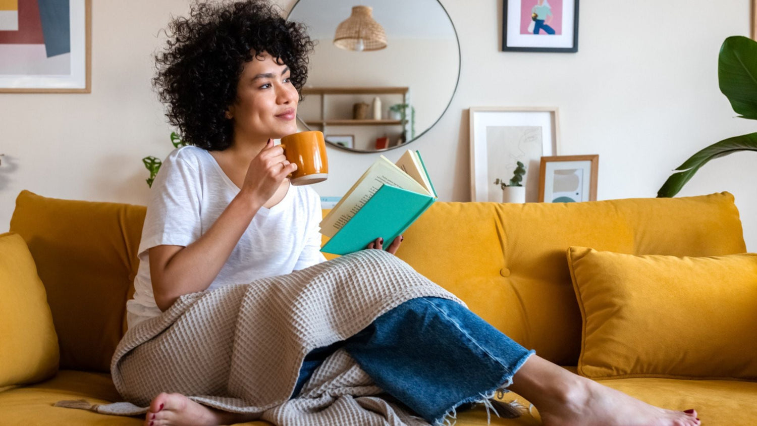 A woman relaxing on a couch drinking coffee and reading a book