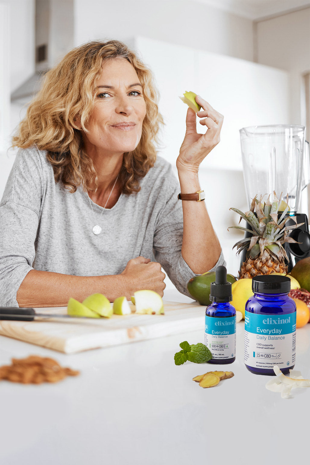 A woman at the kitchen bench cutting and eating fruit along with her Elixinol Everyday Daily Daily Balance products.